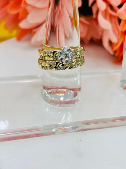Gold wedding rings with diamonds on a clear stand against a blurred floral background